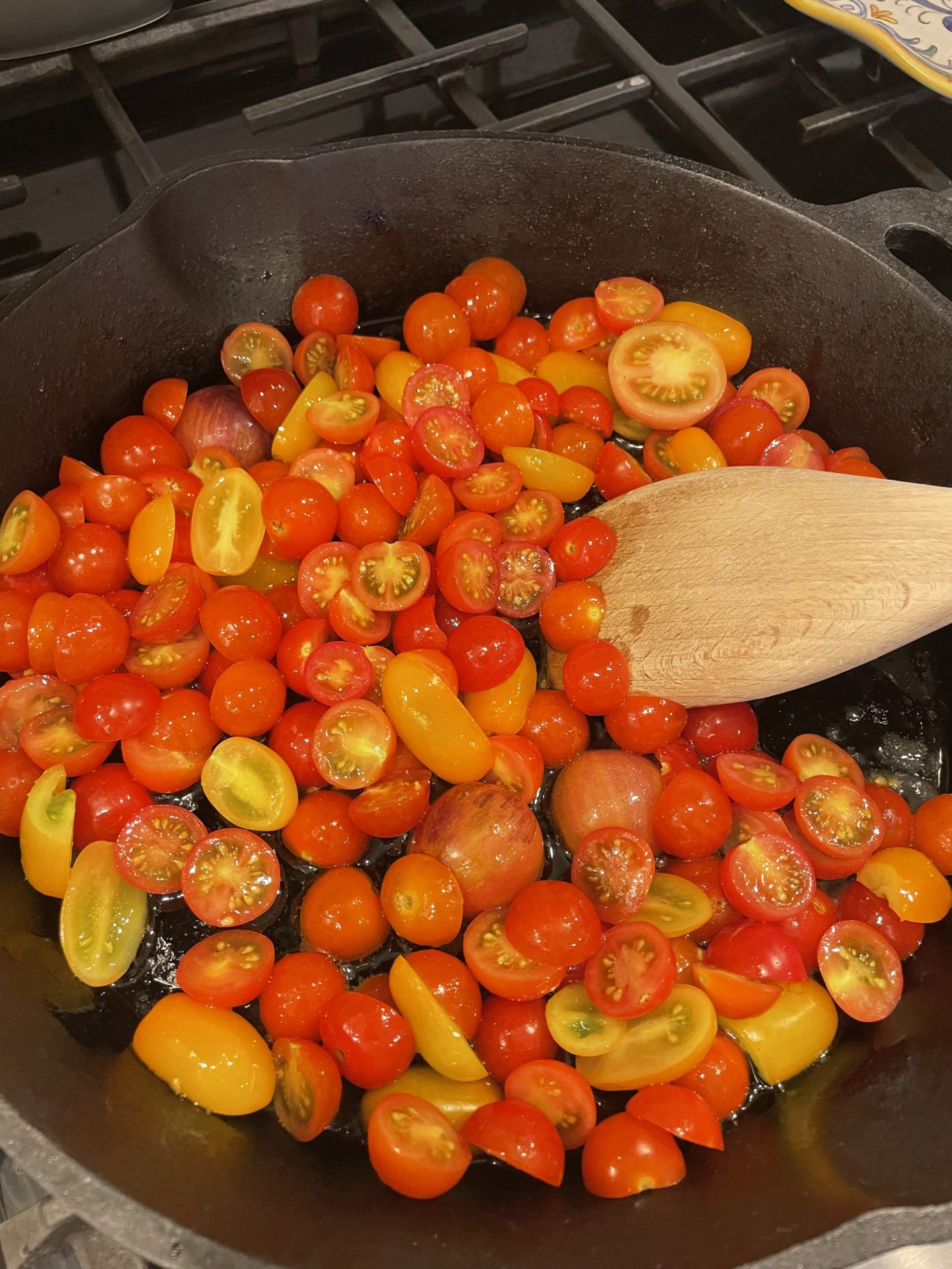 Cherry tomatoes being sauteed in a cast iron pan.