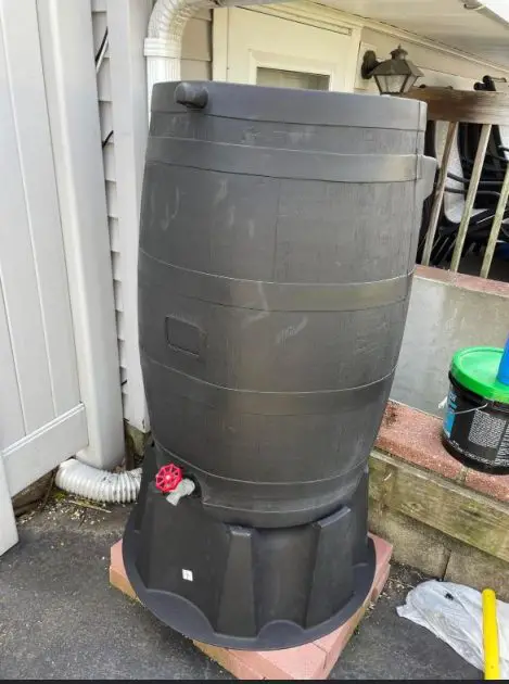 A rain barrel installed. It is brown. In the background is the back of a home.