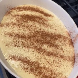 Rice pudding fresh off the stovetop. The container dish it is in is red with a white rim. The background is that of a stovetop.