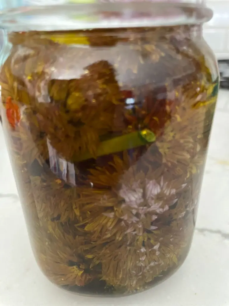 A close up of chive flowers in a jar covered with olive oil.