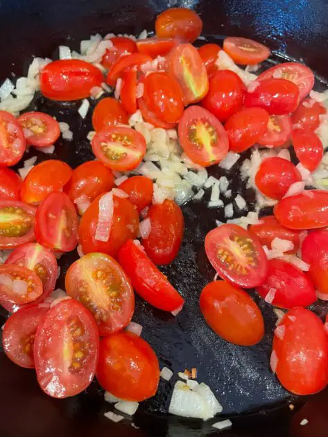 A close up of cherry tomatoes being cooked down with onions.